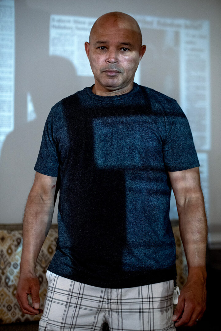 A man standing up with a projection of a newspaper against him.