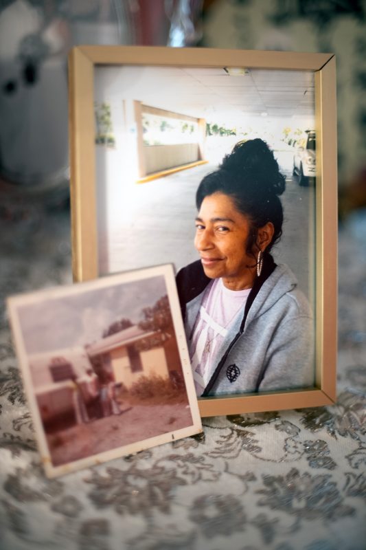 Two photographs: one small photo of people standing in front of a hour, the other larger photo is a portrait of a woman.