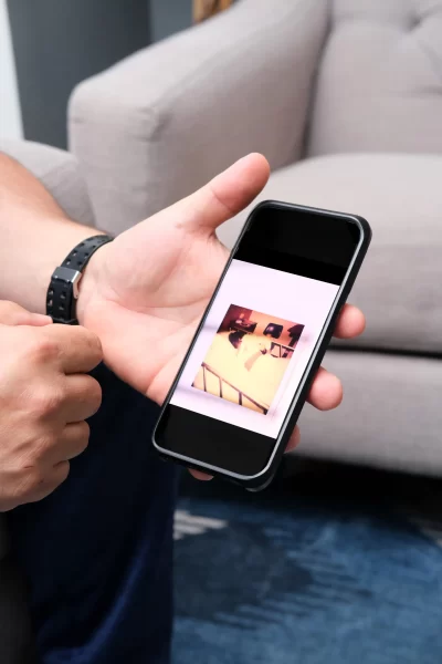 Hands holding up a cell phone with chair in background.