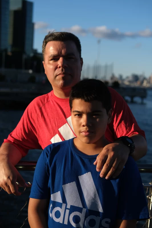 Adult man resting hand on shoulder of younger boy, outside.