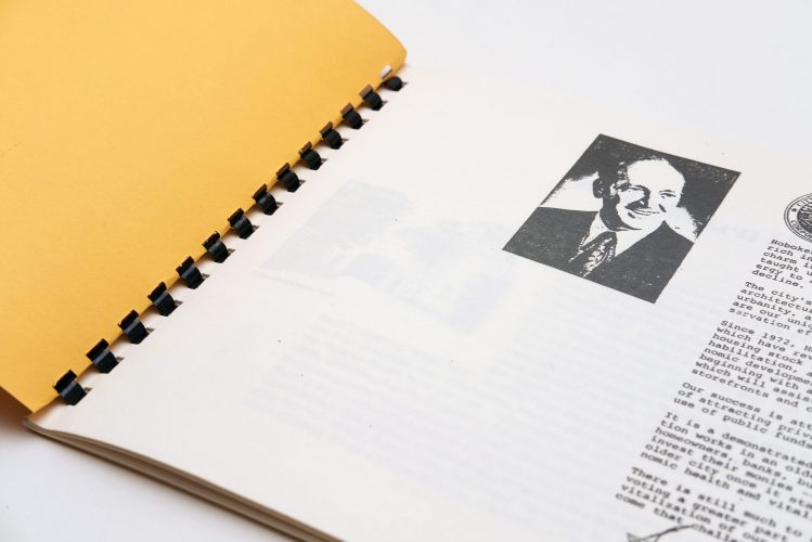An open paper book with a black and white photo of a man smiling on the page.