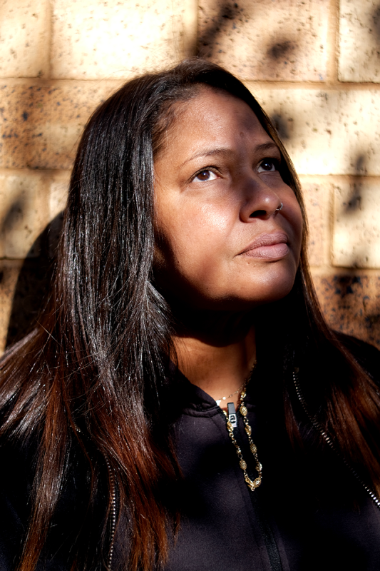 Portrait of a woman with long hair against a brick wall looking up.