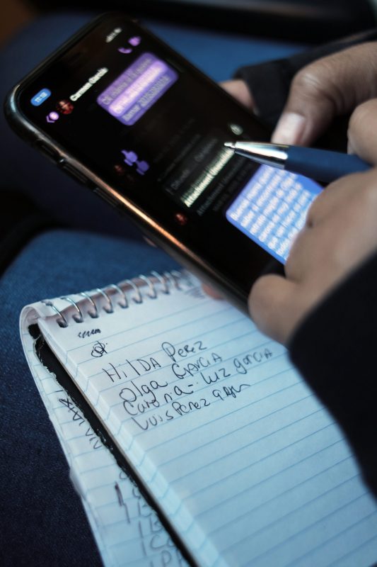 Close up of hands holding a cellphone, pen, and note pad.