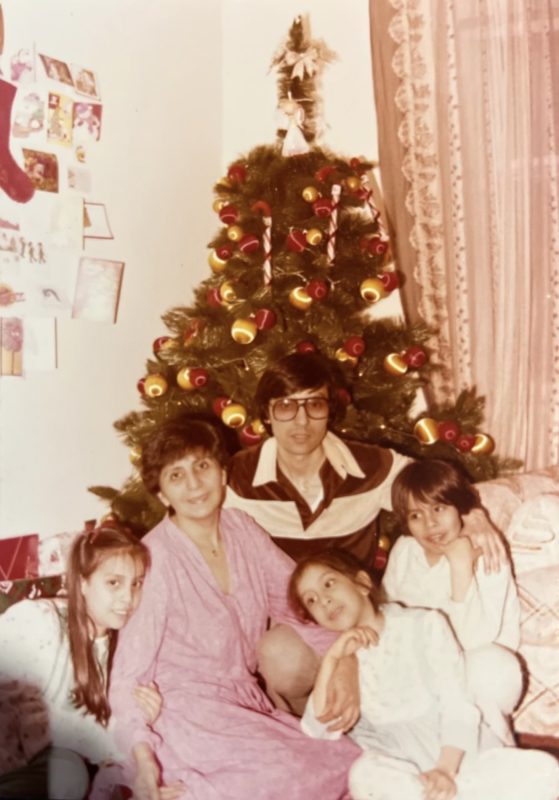 Portrait of two adults and three kids with Christmas tree in background.